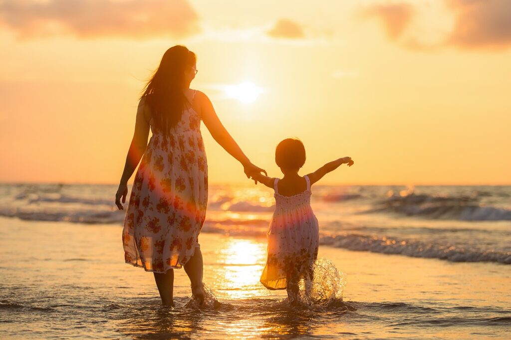 Eine Mutter und ihre Tochter, Privatpersonen, spazieren bei Sonnenuntergang mit Träumen am Strand entlang.